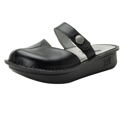 A black Alegria Kamila clog with hand-stitched details, featuring a leather upper and a suede leather footbed, secured with an adjustable hook-and-loop strap and a decorative metal button.