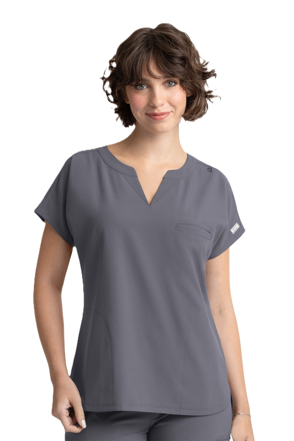 A woman wearing a pewter Maevn Momentum Dolman 3 Pocket Scrub Top with a notched neckline, dolman sleeves, and side pockets.